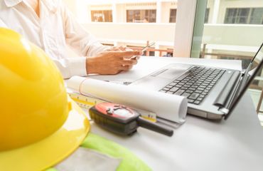 Hard hat and tools beside a laptop and blueprints on a desk at a construction site office Hard hat and tools beside a laptop and blueprints on a desk at a construction site office