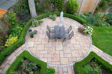 Circular stone patio with outdoor dining table, umbrella, and chairs in a landscaped garden Circular stone patio with outdoor dining table, umbrella, and chairs in a landscaped garden