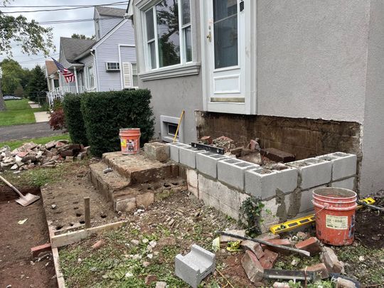House exterior with a partially built concrete block foundation and construction tools in a yard House exterior with a partially built concrete block foundation and construction tools in a yard