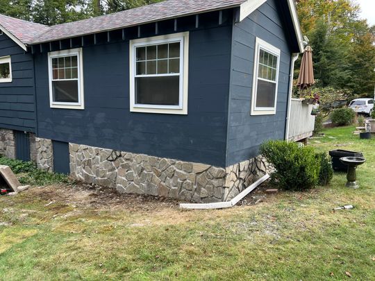 Dark blue house with stone foundation, white-trimmed windows, and a small yard. Dark blue house with stone foundation, white-trimmed windows, and a small yard.
