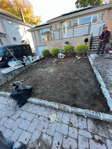 Front yard landscaping with stone border, fresh soil, potted shrubs, and a person standing by the steps