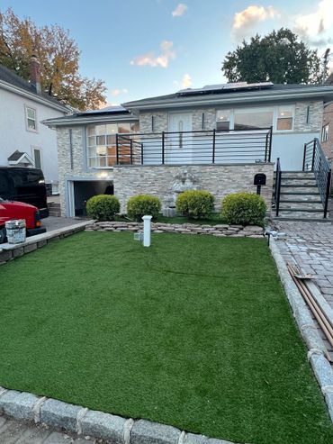 Backyard patio with green lawn, stone steps, and a white house with a balcony and shrubs Backyard patio with green lawn, stone steps, and a white house with a balcony and shrubs