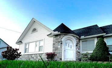 White suburban house with stone facade, dark roof, and front lawn under a blue sky