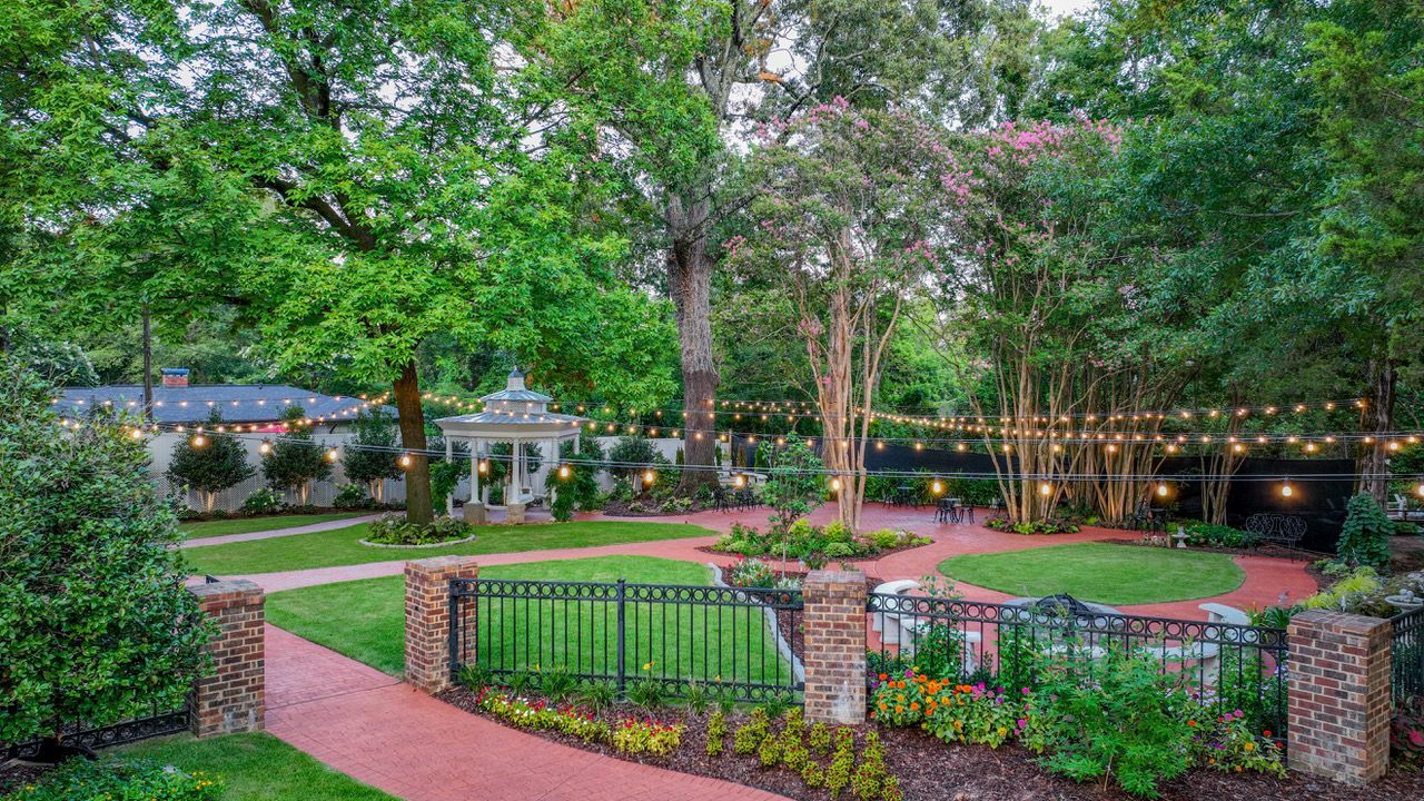 A large lush green garden with a brick walkway leading to a house.