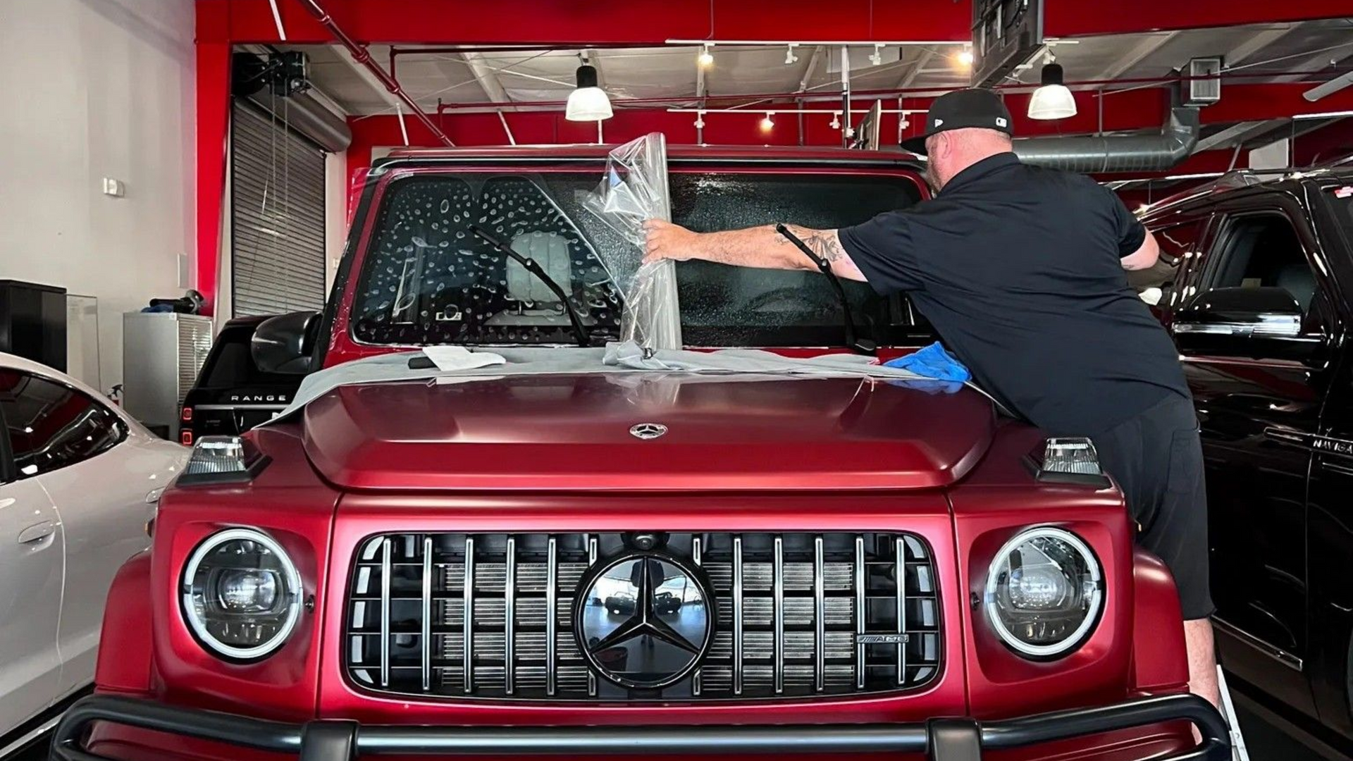 Person washing a red Mercedes SUV inside a car detailing shop