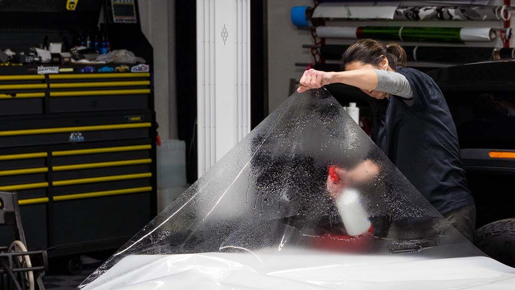 Person spraying a car windshield with water in a garage, creating a splash near the hood
