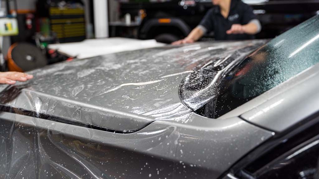 Close-up of a silver car being wrapped in clear protective film in a workshop
