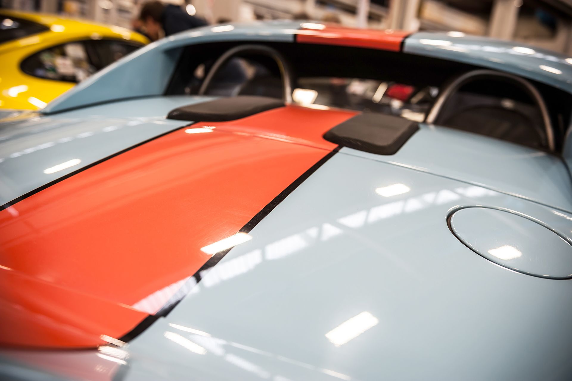 Close-up of a light blue sports car with a red racing stripe and rear spoiler in a showroom