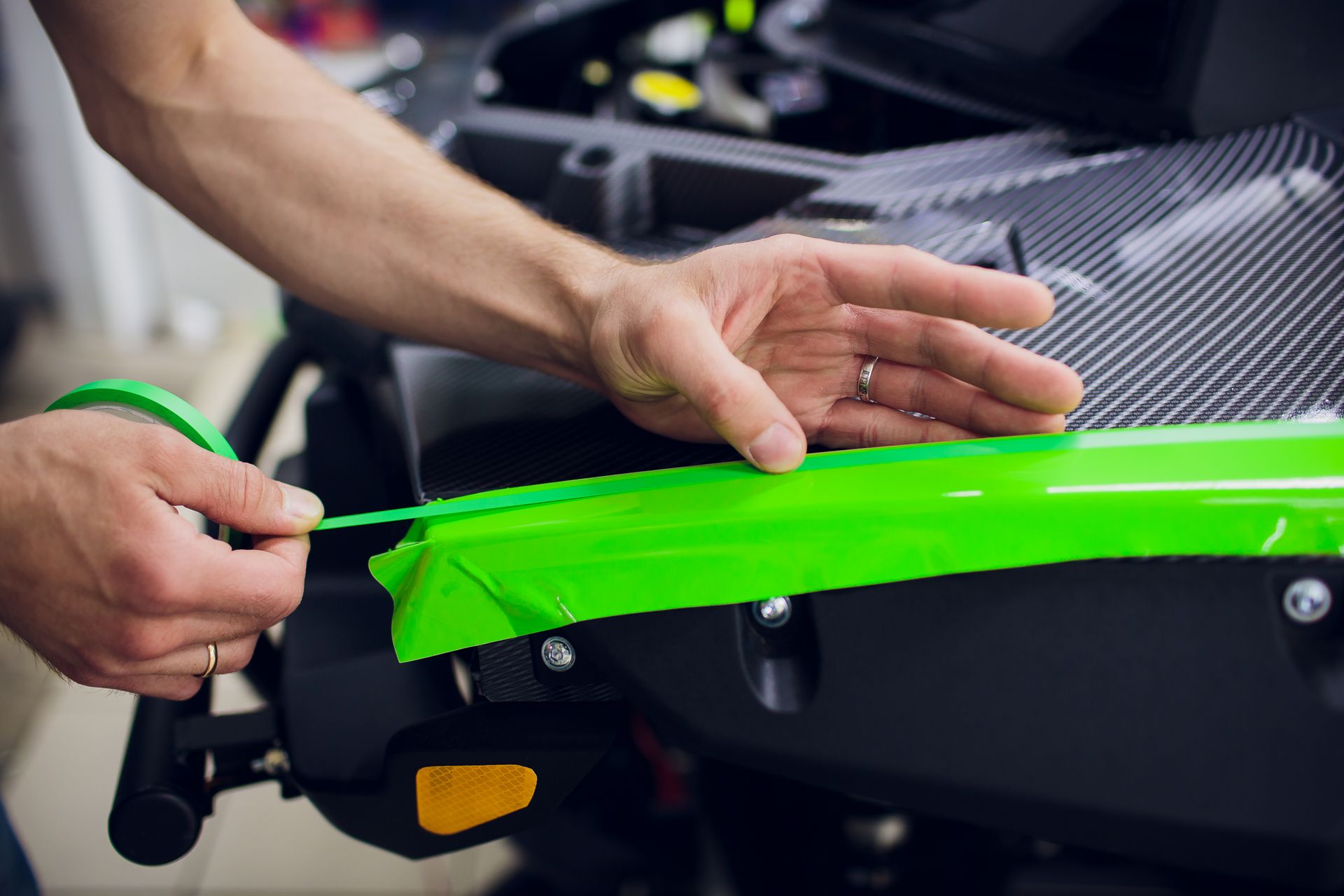 Hands applying bright green vinyl wrap to a car body panel in a workshop