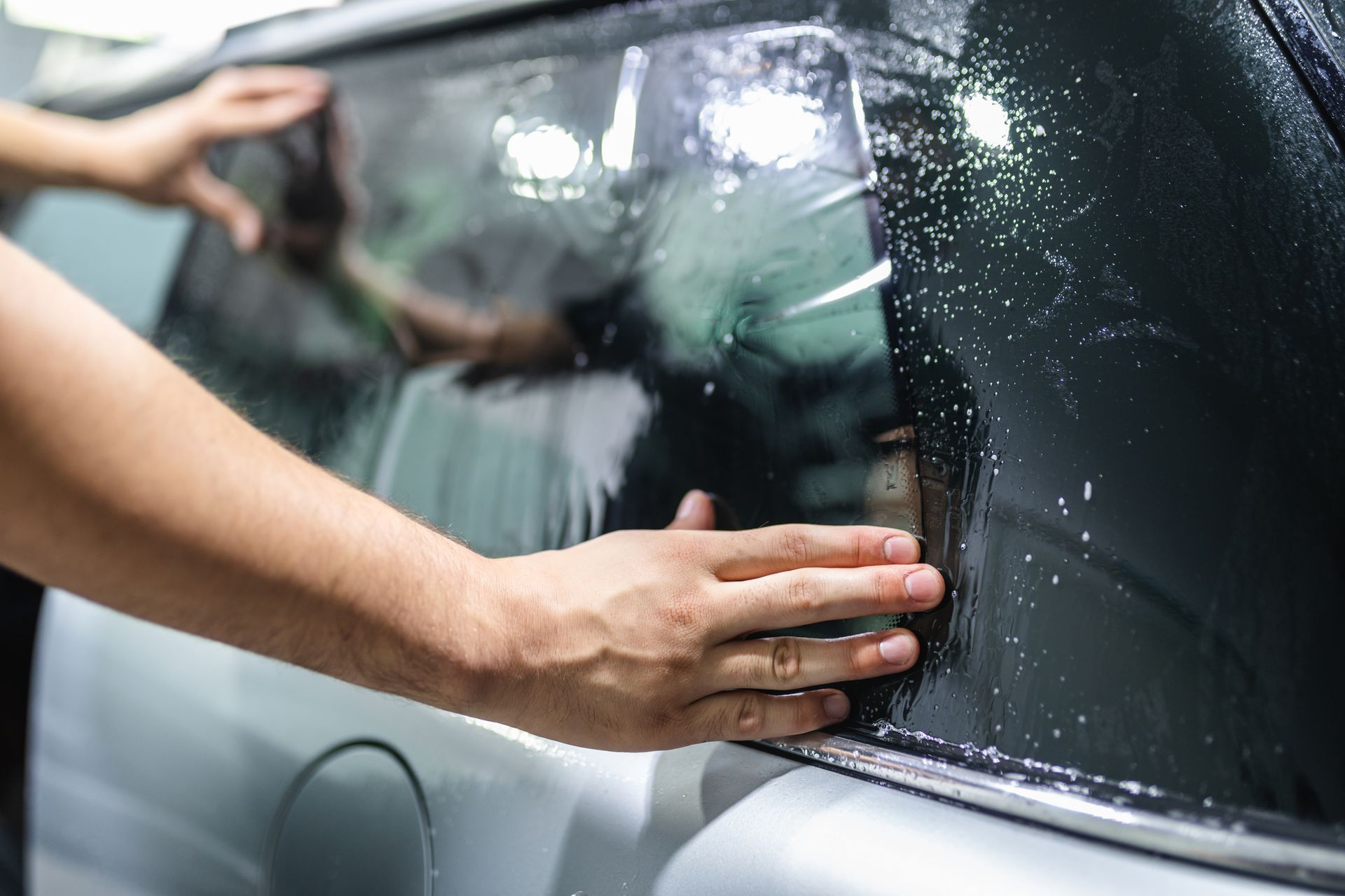 Person cleaning a car window with a cloth, wiping away water droplets.