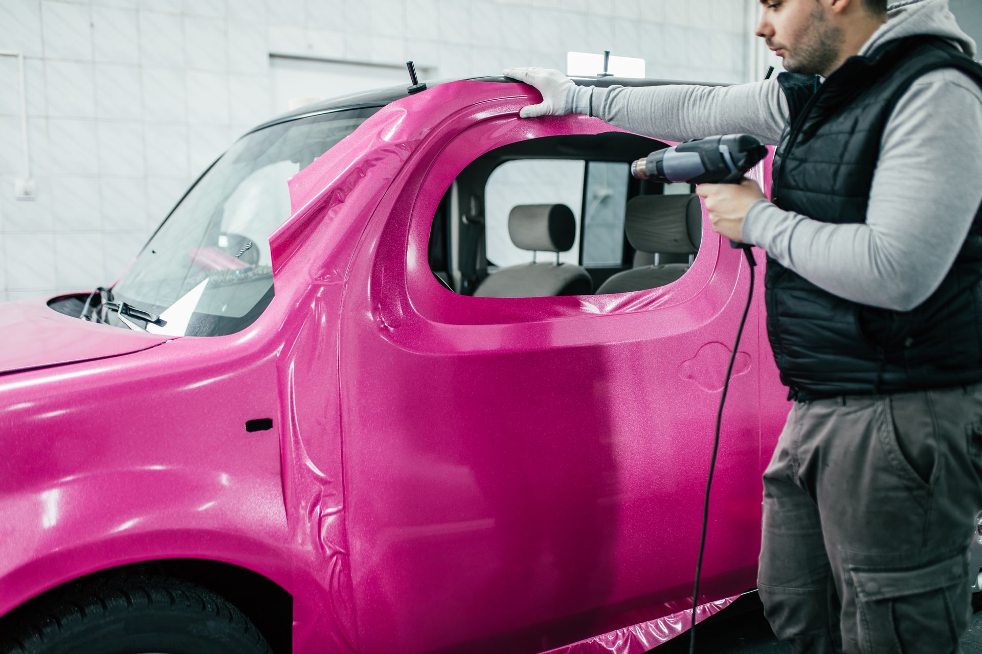 Man spray-painting a bright pink car body in a workshop