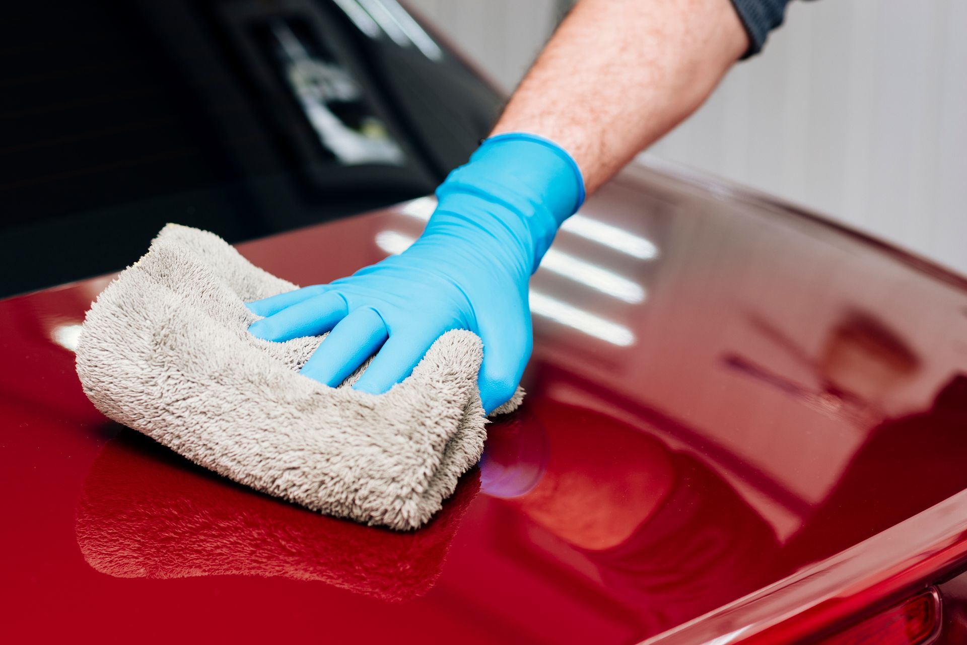 Gloved hand wiping a red car hood with a microfiber cloth