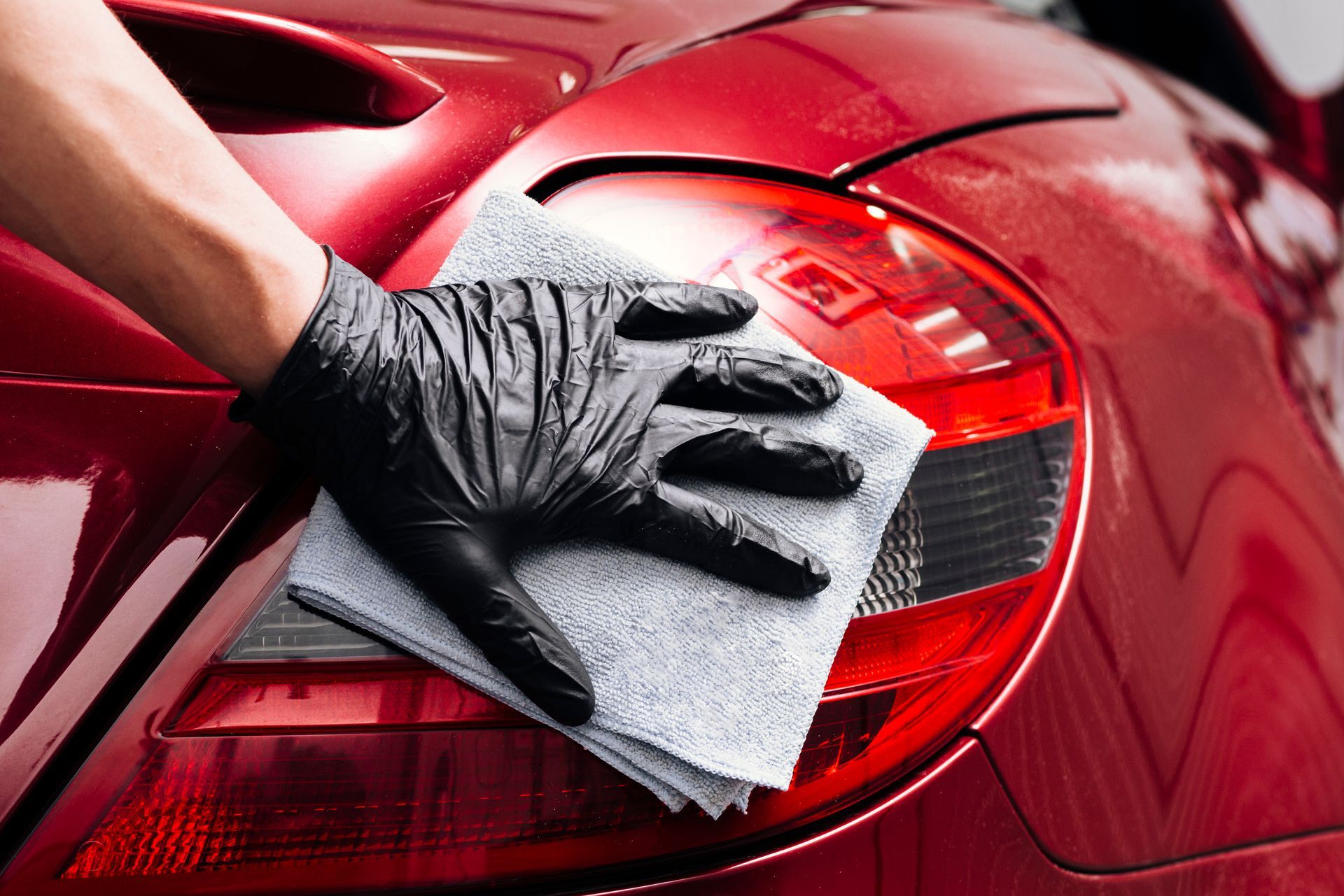 Gloved hand polishing a red car’s taillight with a gray cloth