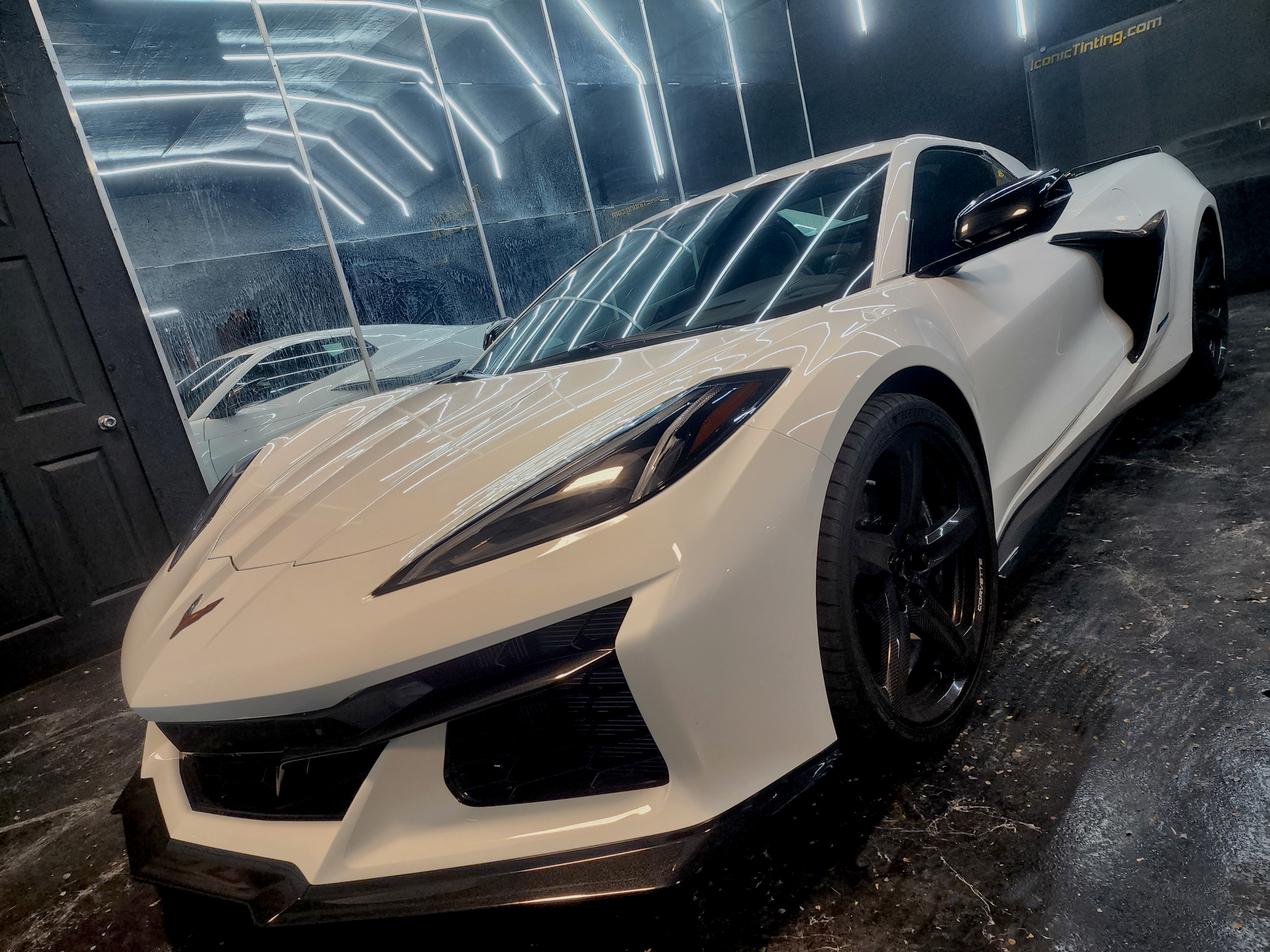 White sports car with black wheels parked under bright lights in a garage