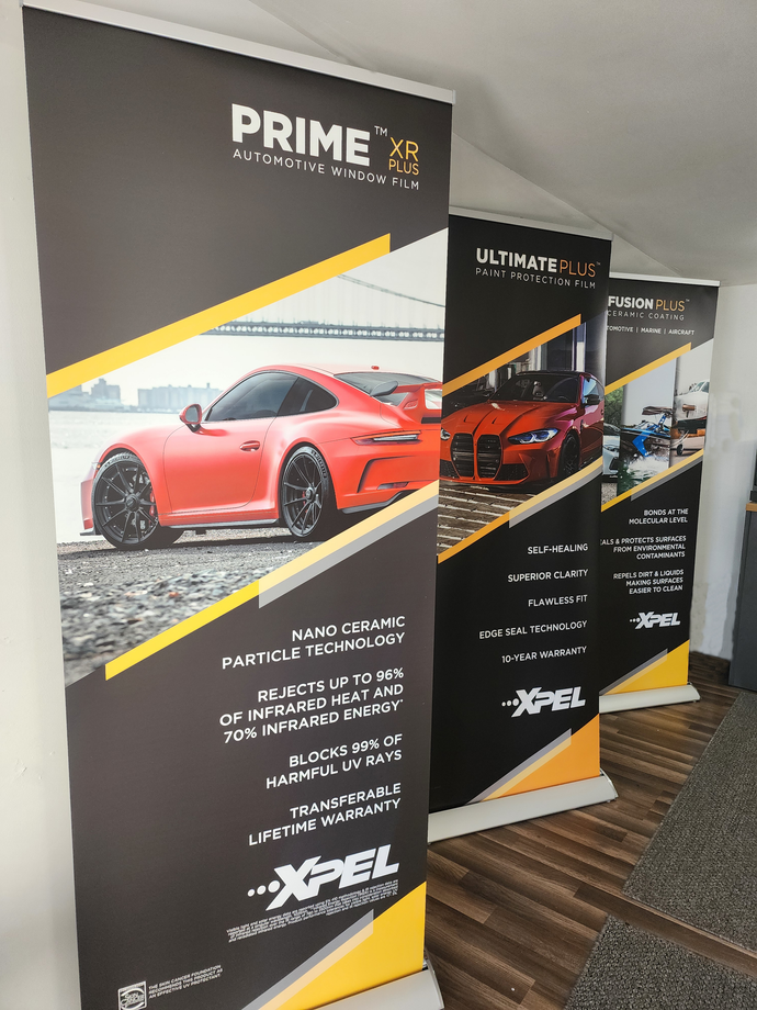Two black promotional banners with sports cars, including a red car, in an indoor hallway.