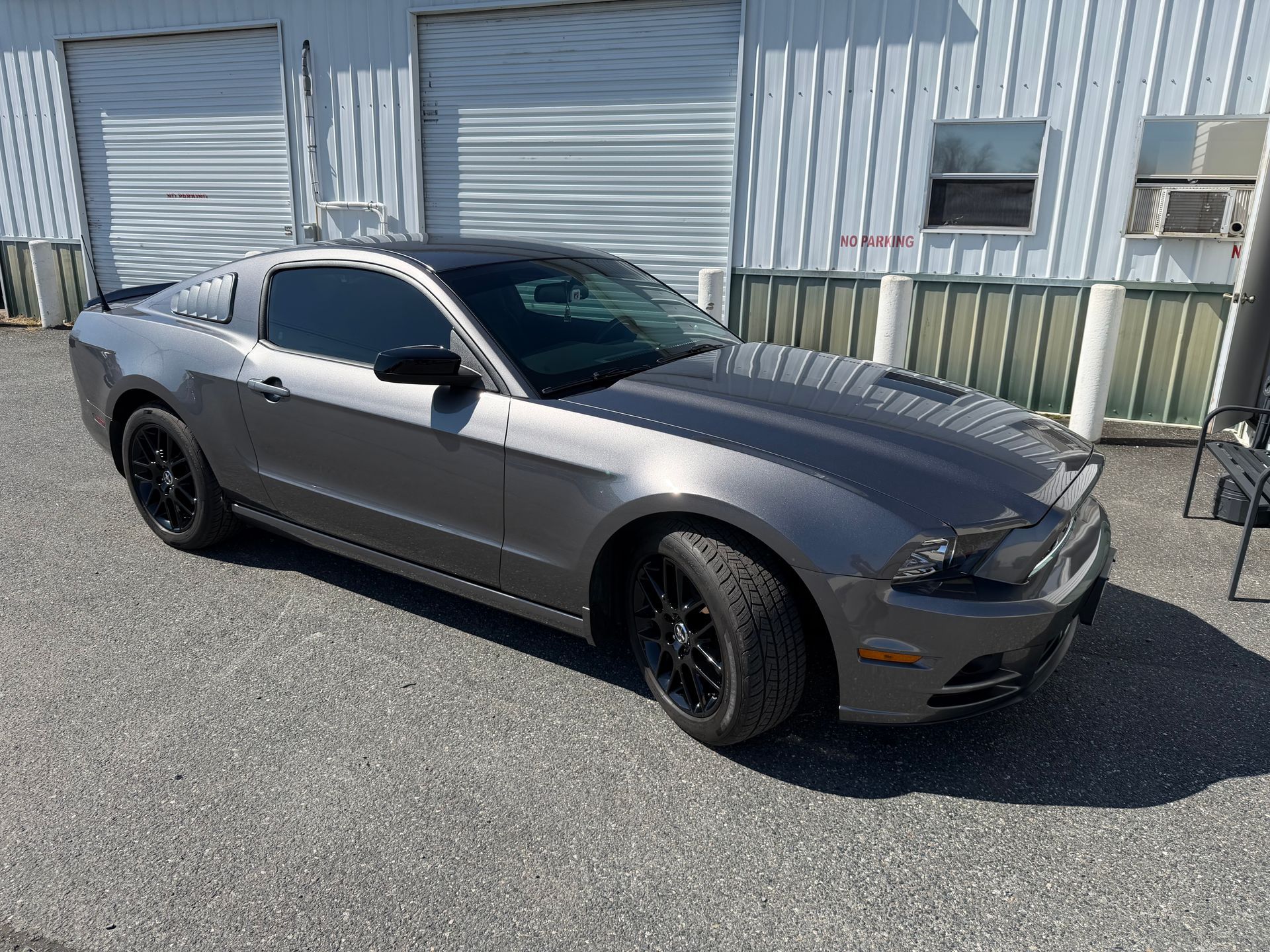 Gray sports car parked outside an industrial building with roll-up doors