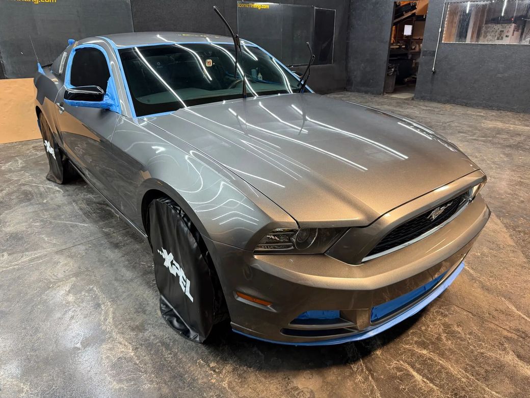 Gray Ford Mustang with blue accents, parked indoors on a concrete floor.