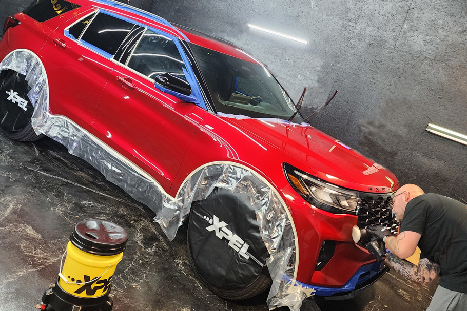 Red car being washed with soap in a car wash, with a bucket and hose nearby.