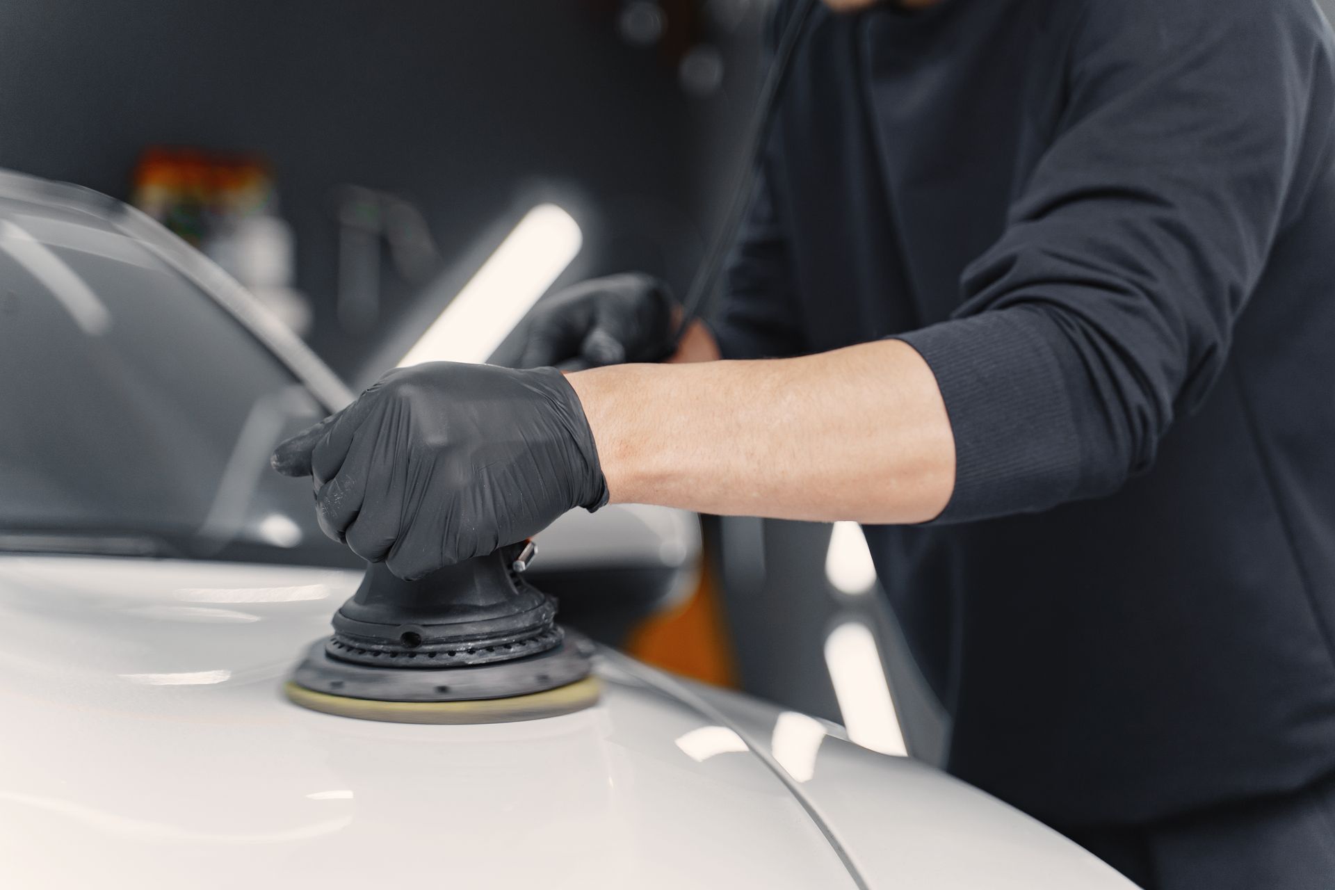 Person polishing a white car hood with a buffer in a detailing shop