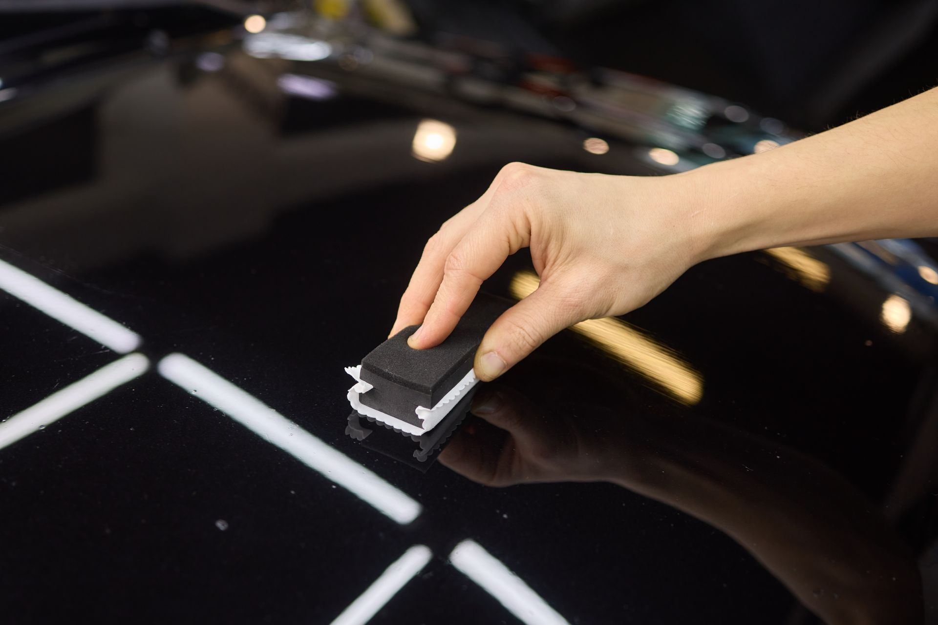 Hand polishing a glossy black car hood with a small sponge.