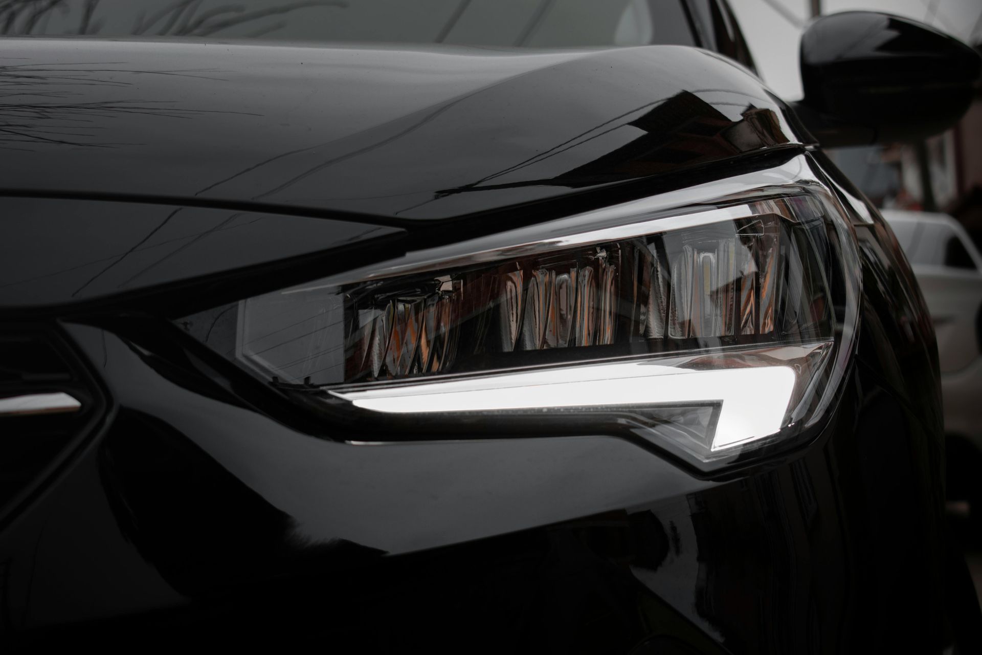 Close-up of a black car’s front headlight with a glossy hood reflection