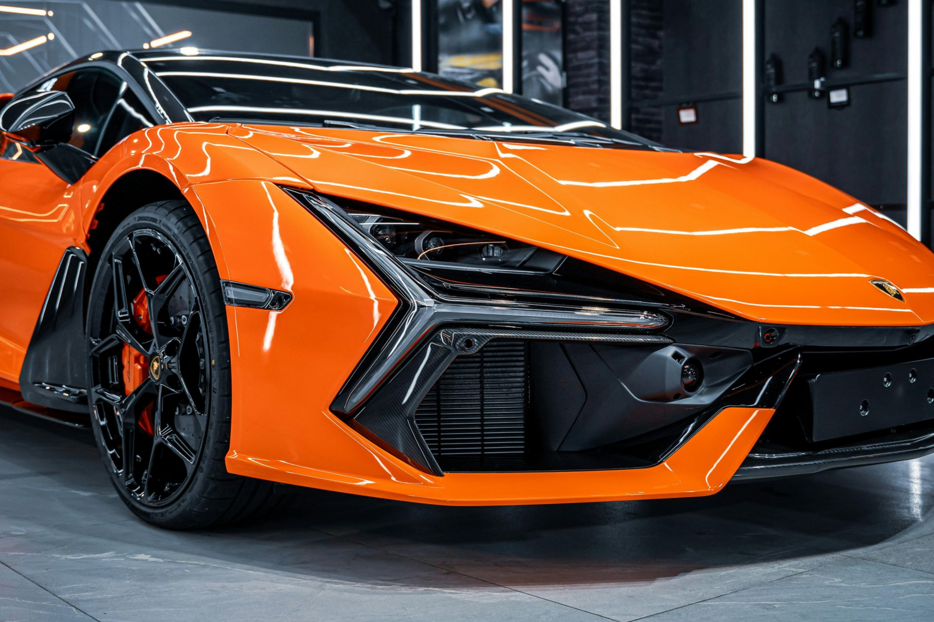 Orange sports car in a garage, low-angle front view with black accents and sleek aerodynamic styling