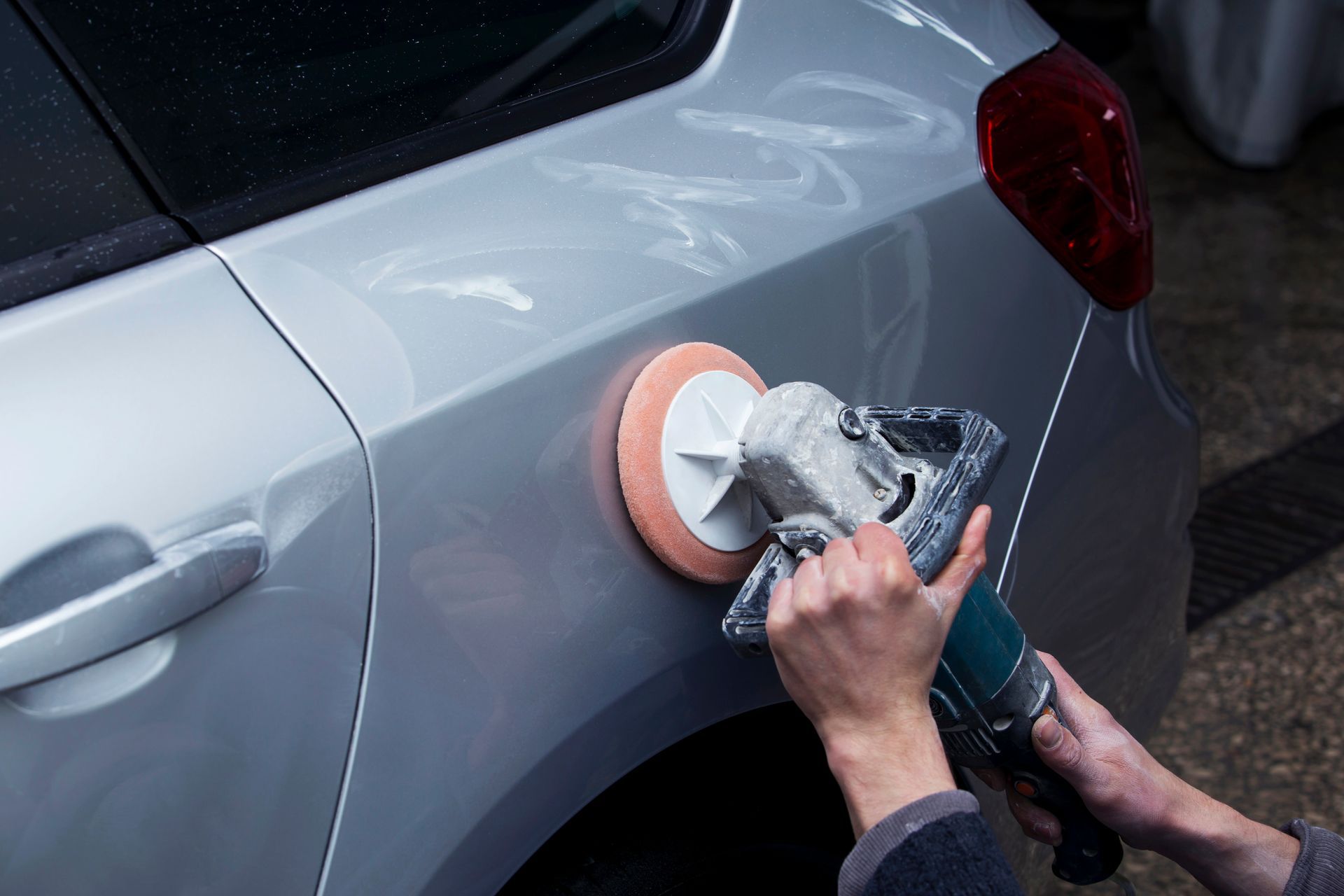 Person polishing a silver car door with a buffer in a garage
