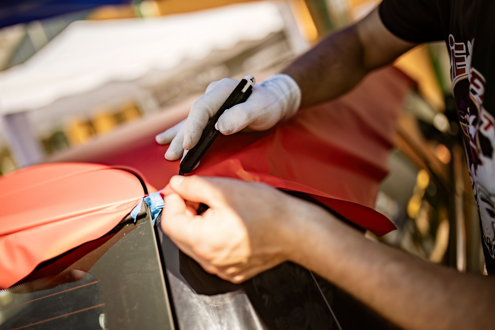 Person wearing gloves repairs a red metal surface with a screwdriver outdoors