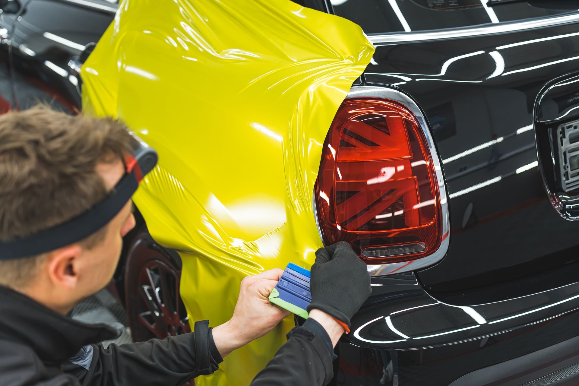 Technician applying yellow film to a black car taillight in an auto shop