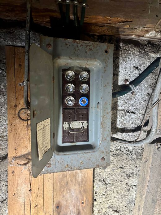 Open electrical breaker panel with exposed wiring mounted on a wooden post indoors
