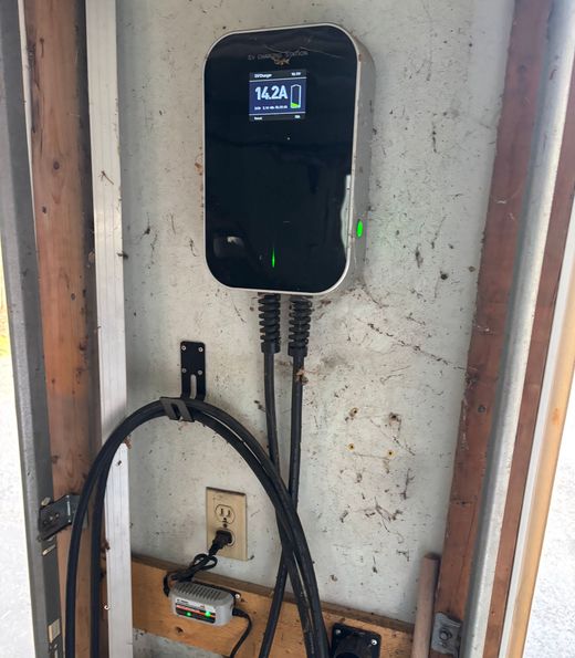 Black EV charger mounted on a wall with connected cable in a utility area.