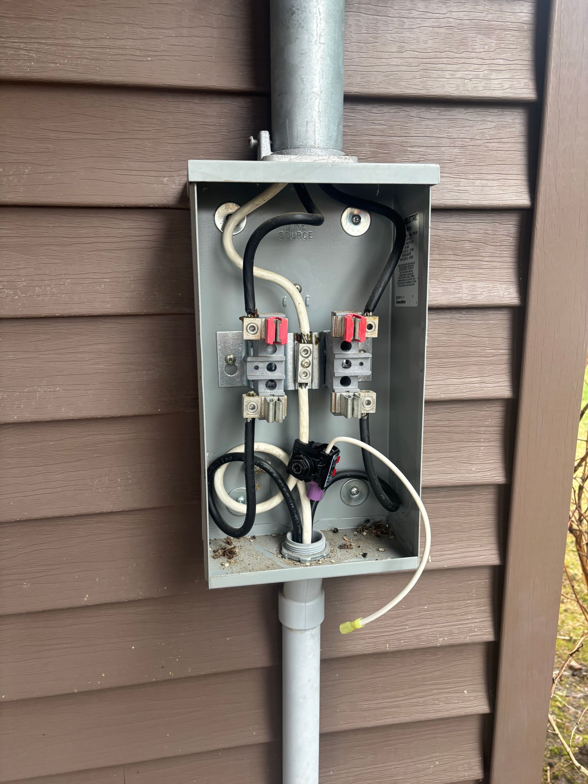 Open electrical service box with wires and meter components mounted on an exterior wall.