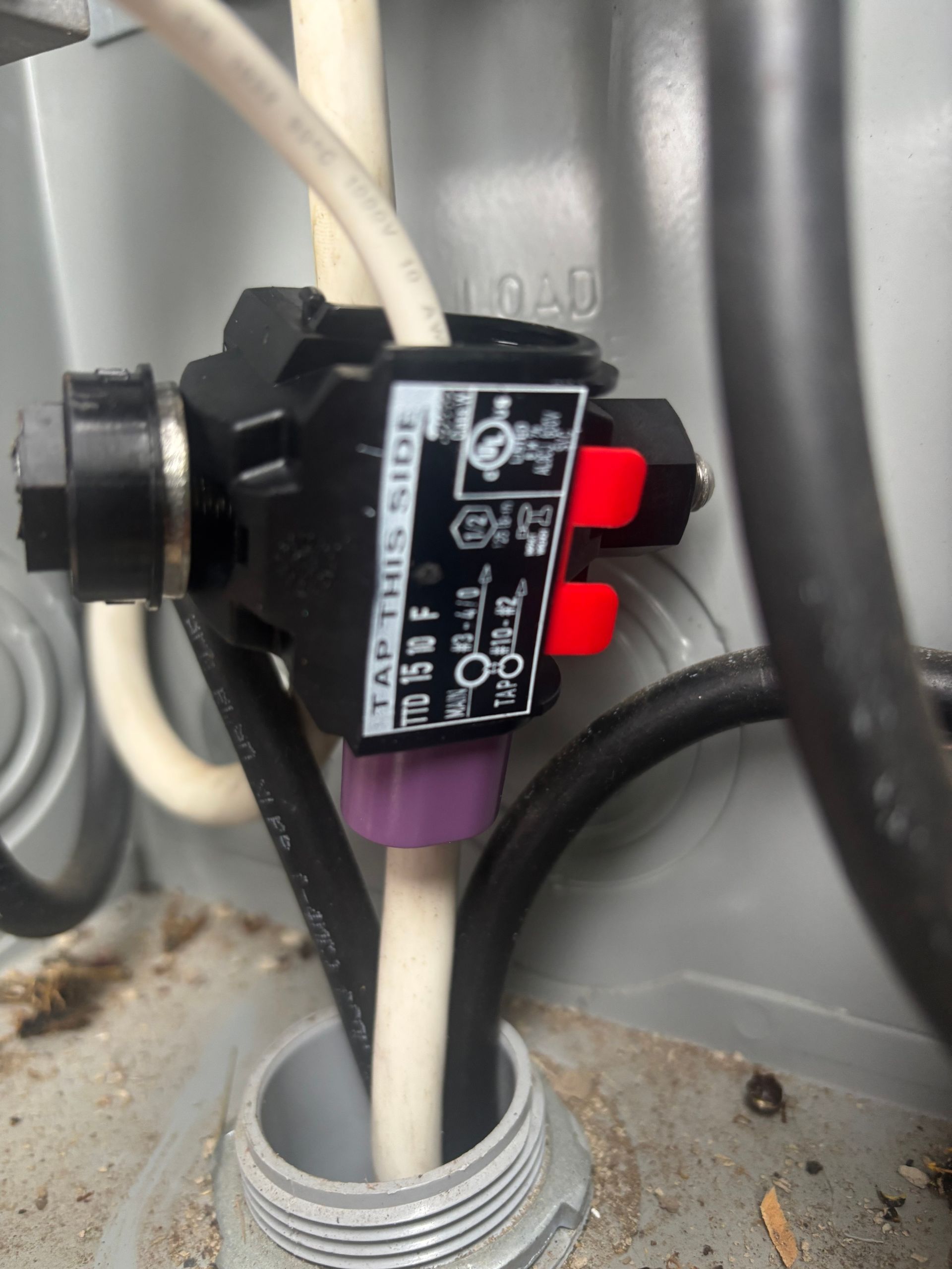 Black electrical sensor switch with red tabs and white cable mounted on a gray metal panel