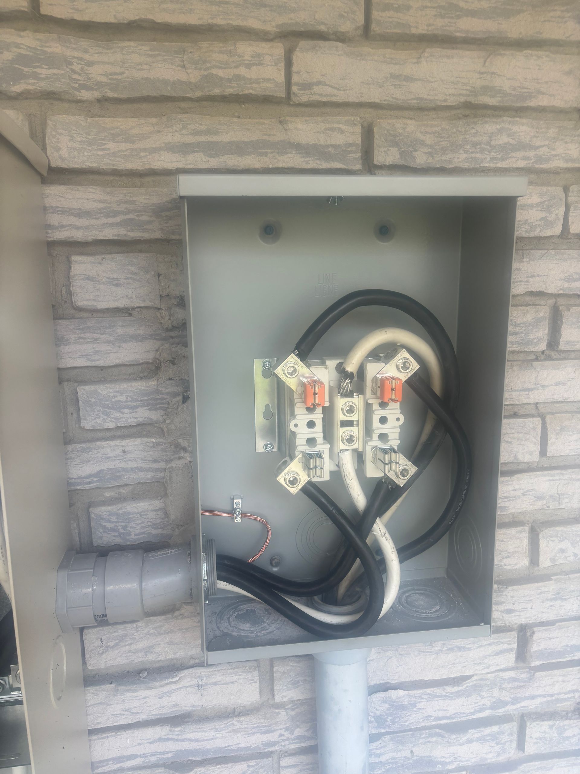 Open electrical panel in a stone wall with visible wiring and terminal blocks