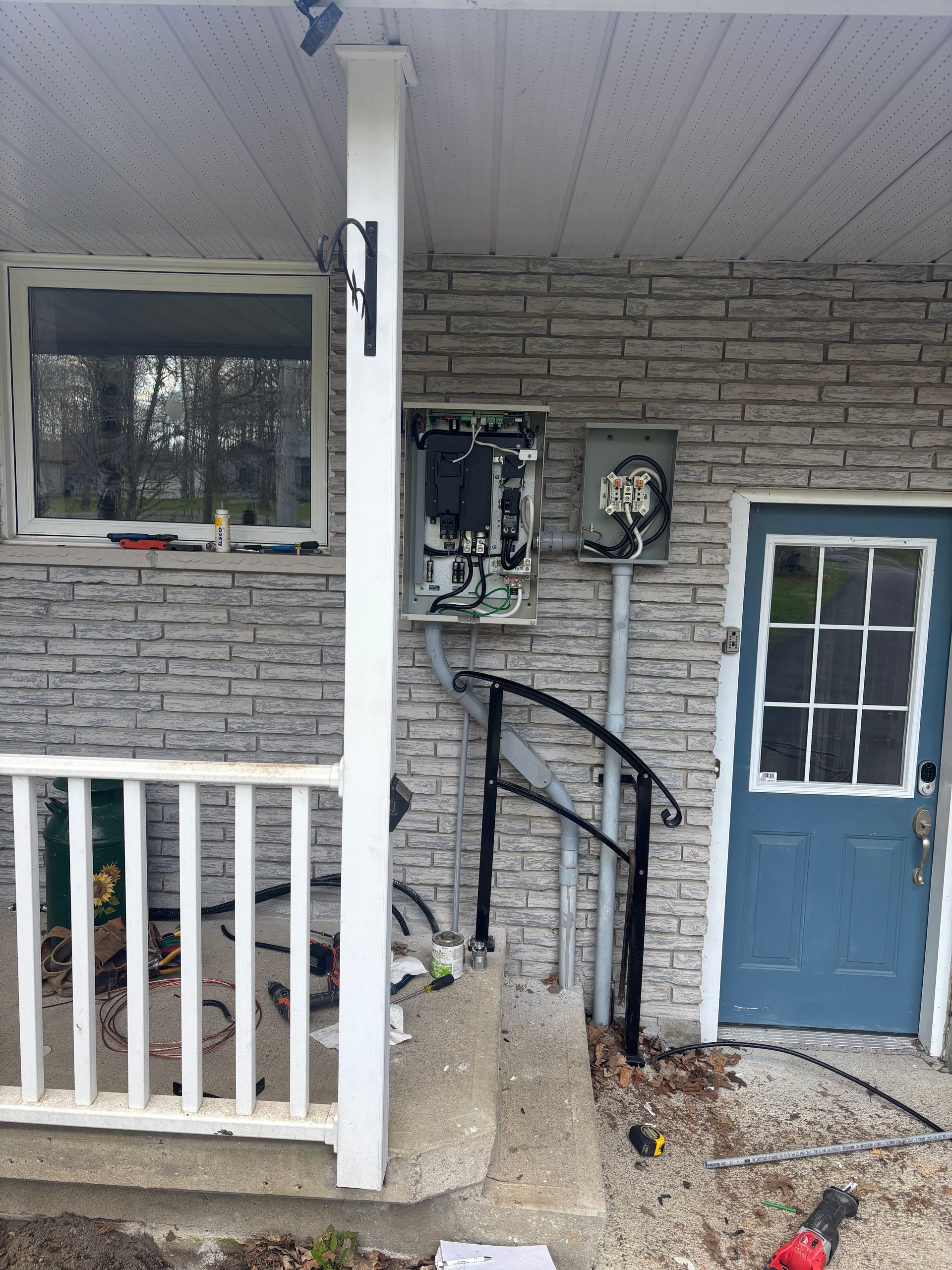 Front porch with blue door, white railing, utility meter, and stone wall siding