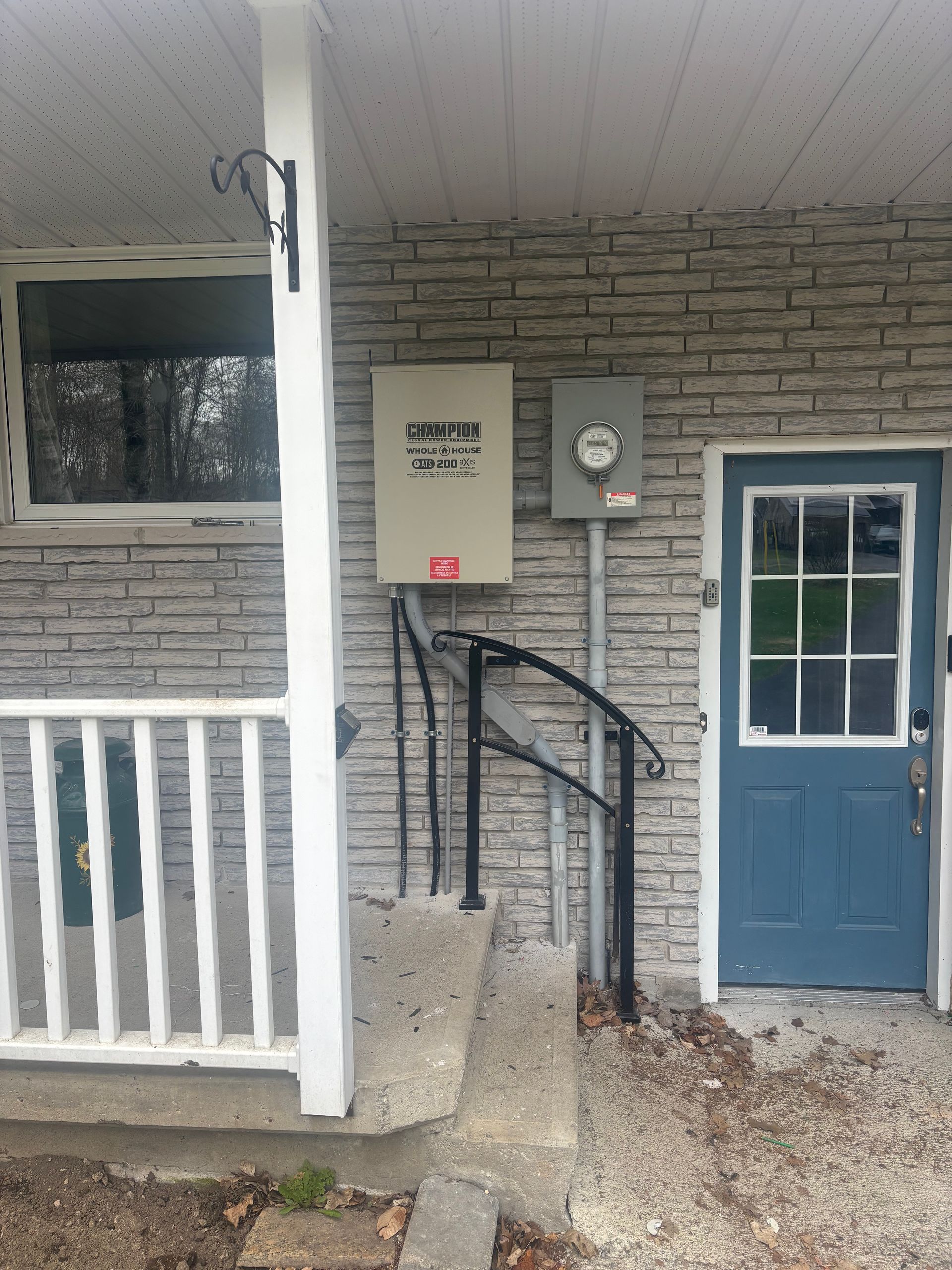 Front porch with blue door, gray brick wall, ramp, and white railing under a covered entrance