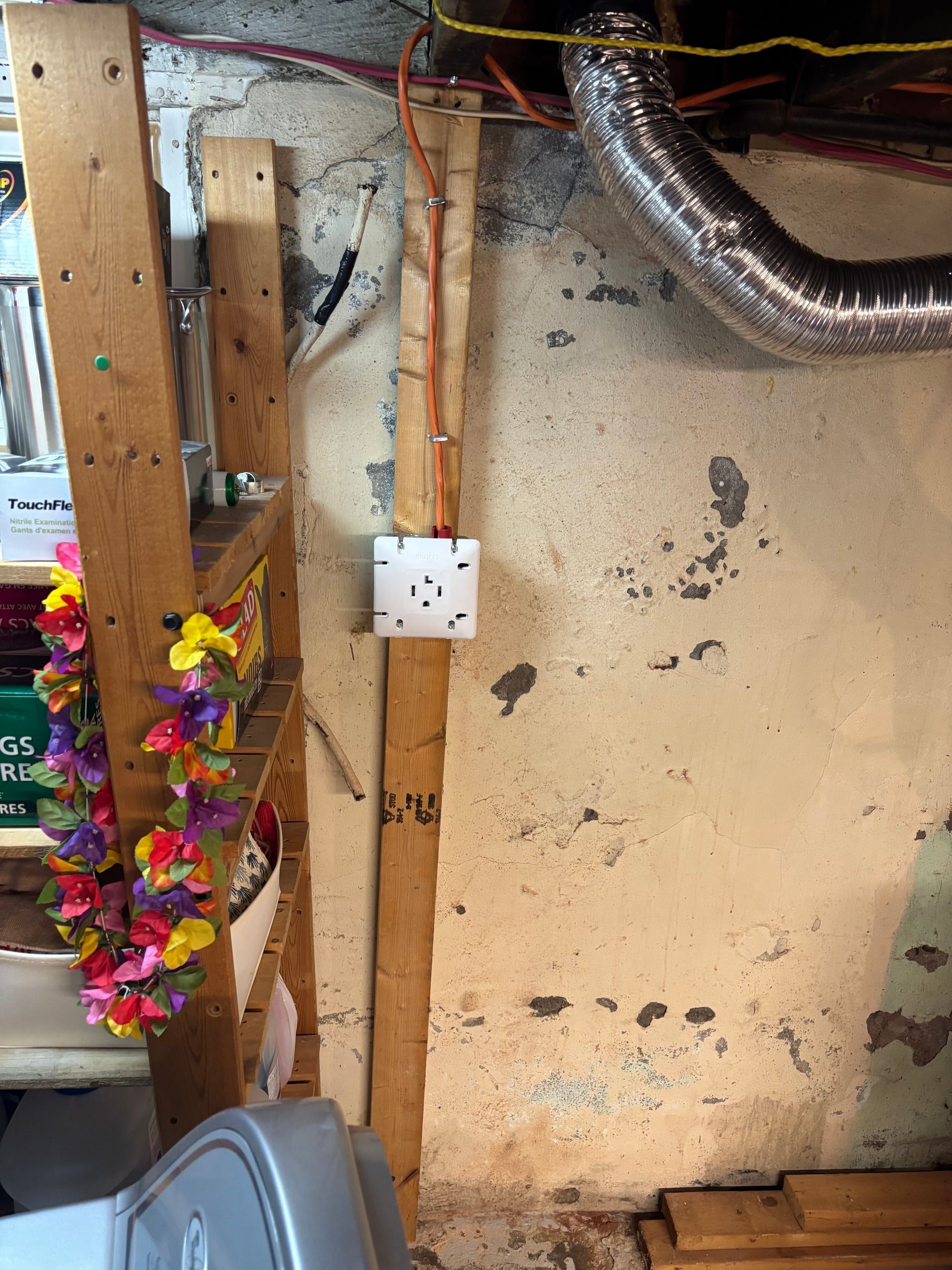 Basement wall with exposed wiring, a white outlet box, hanging garland, and silver ducting overhead