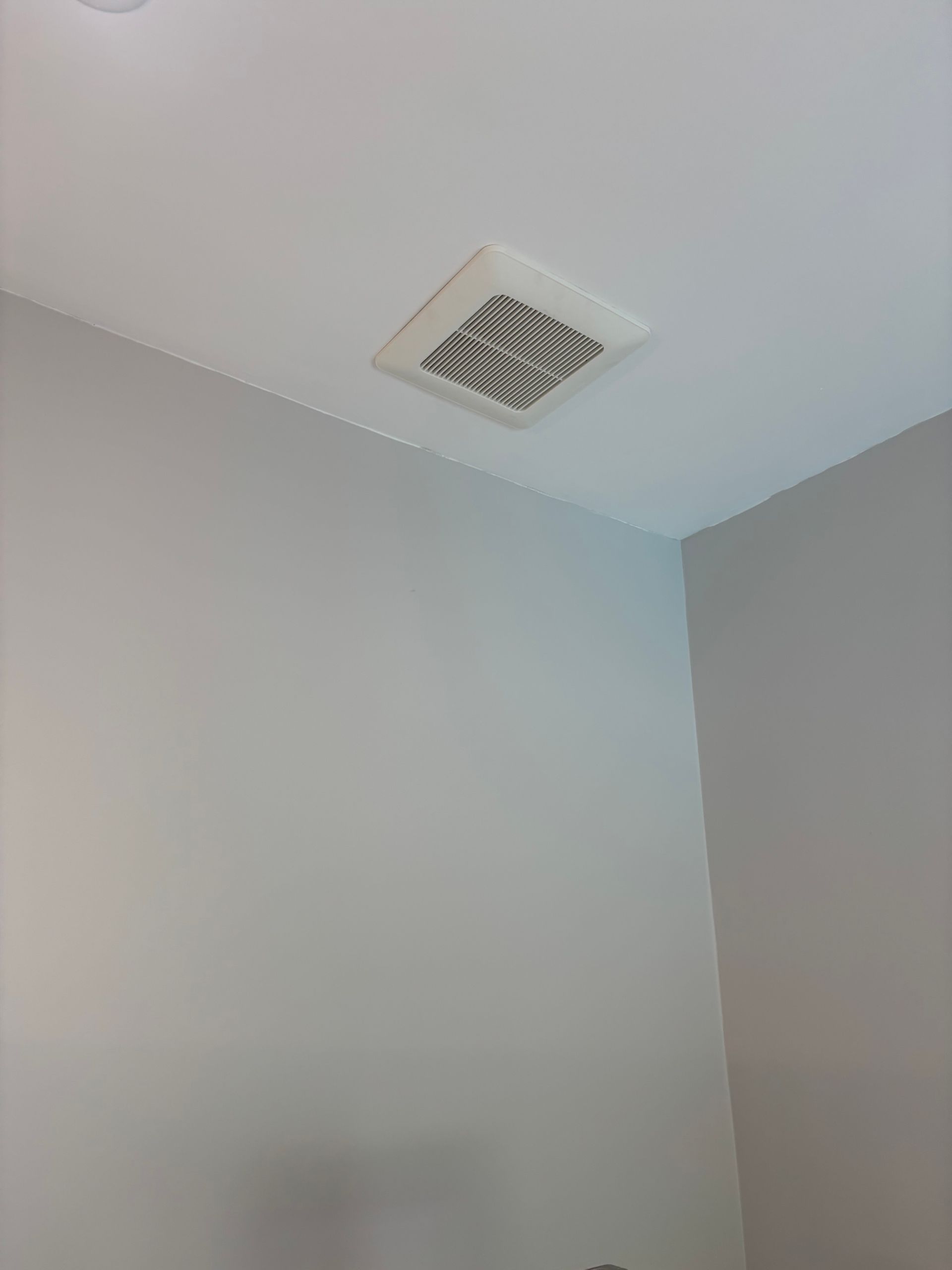 Corner of a light gray room with a white ceiling vent near the top.