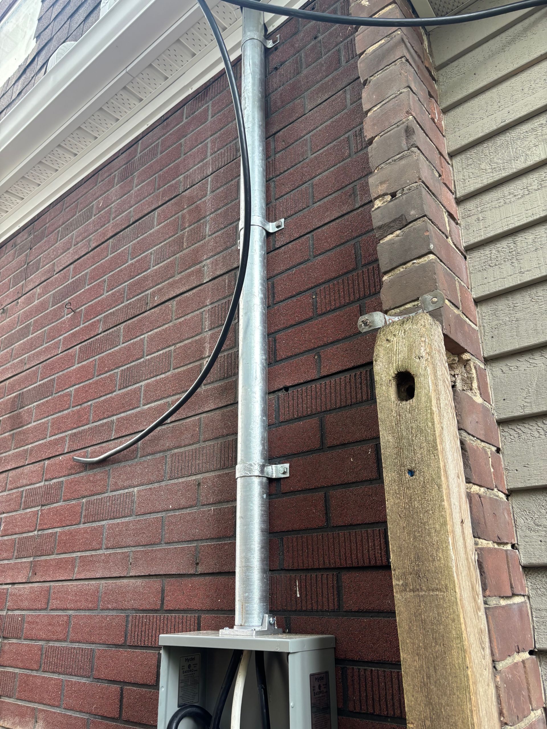 Metal conduit and cables on a brick building corner beside a utility box and weathered wooden post.