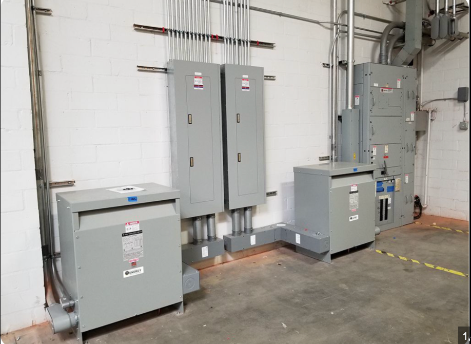 Electrical equipment cabinets and control panels in an industrial utility room with gray walls and concrete floor