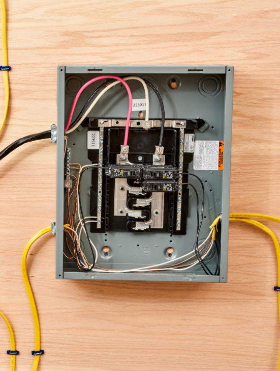 Open electrical breaker panel with exposed wiring on a wooden wall.