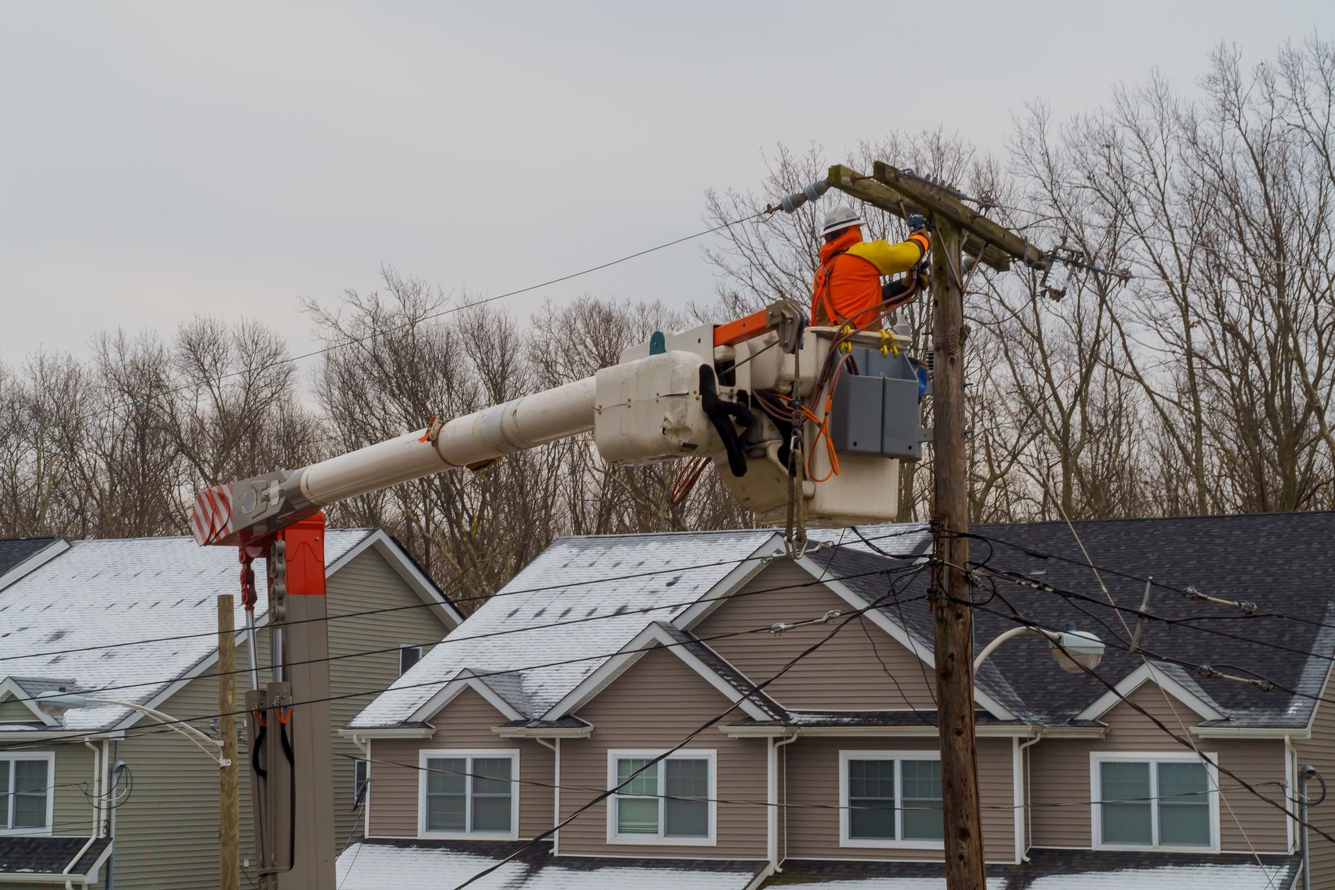 Utility workers repairing power lines from a bucket lift above snowy rooftops.
