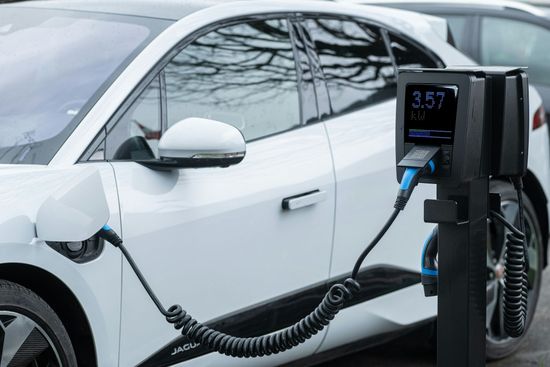 Electric car plugged into a charging station outdoors, with a white vehicle and visible charging cables