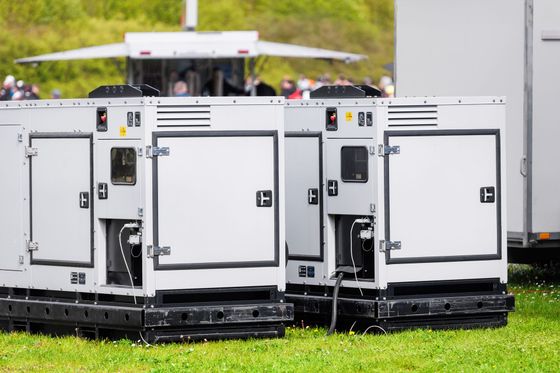 Two white portable generator units on black skids sitting on grass outdoors.
