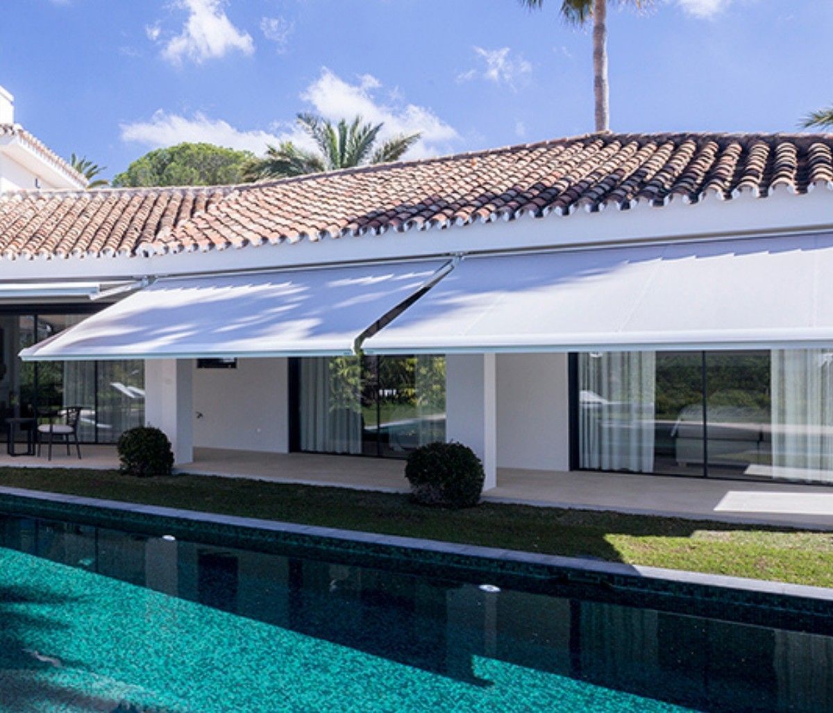 Casa moderna con tetto in tegole, tende da sole retrattili e piscina antistante.