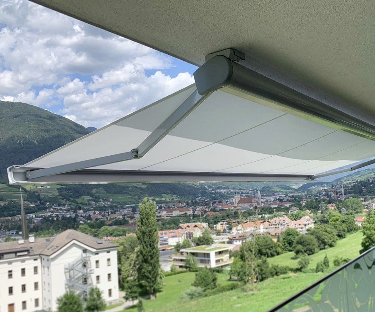 Tenda da sole retrattile per balcone, che si estende su una vista panoramica della città e delle montagne.