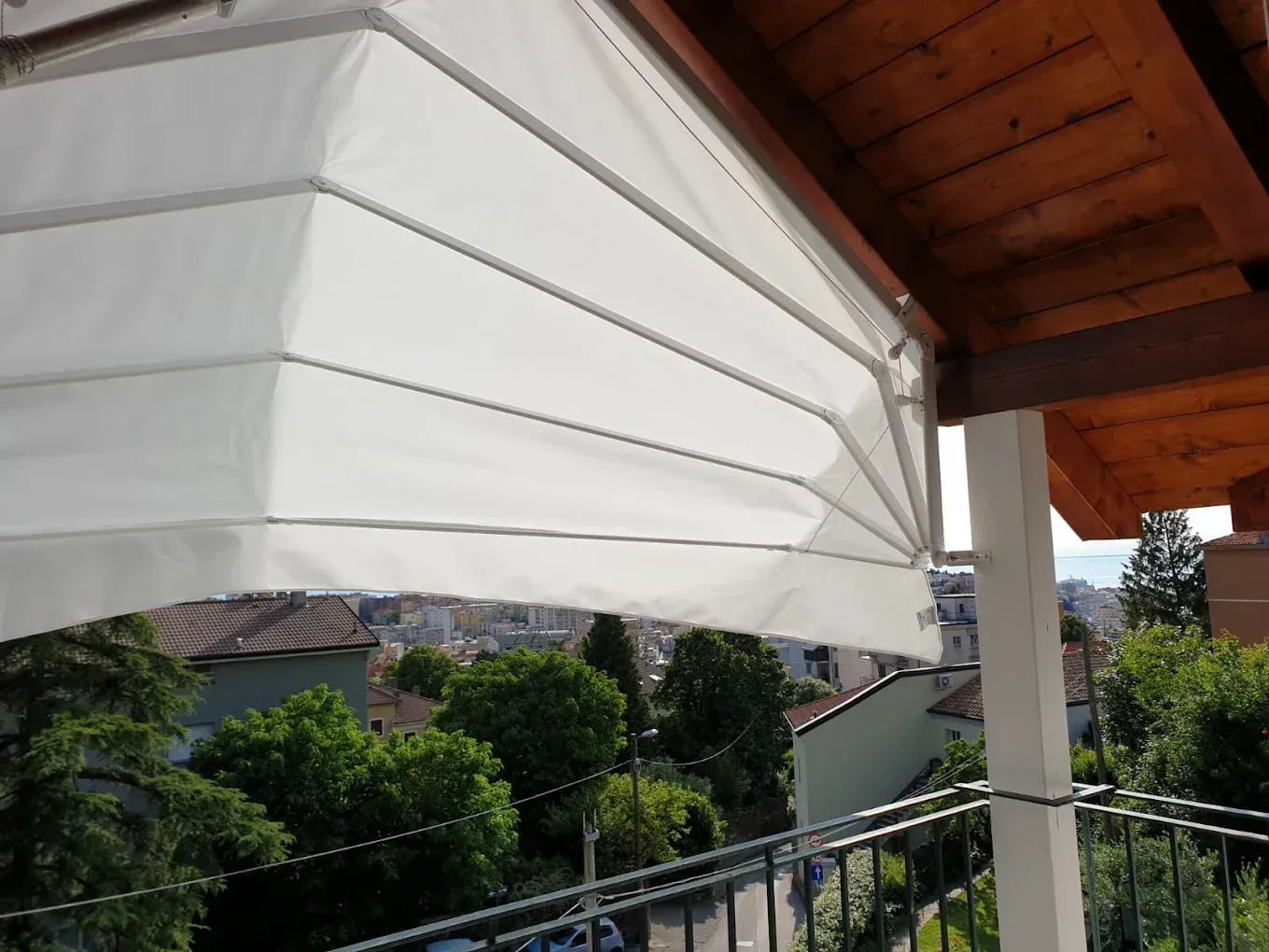 Tenda a righe bianche sopra un balcone, con vista su verdi colline e tetti.