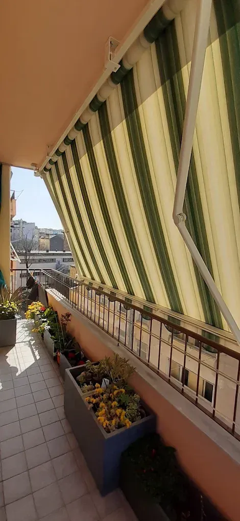 Balcone con tenda a righe verdi e bianche, piante in vaso e vista sulla città