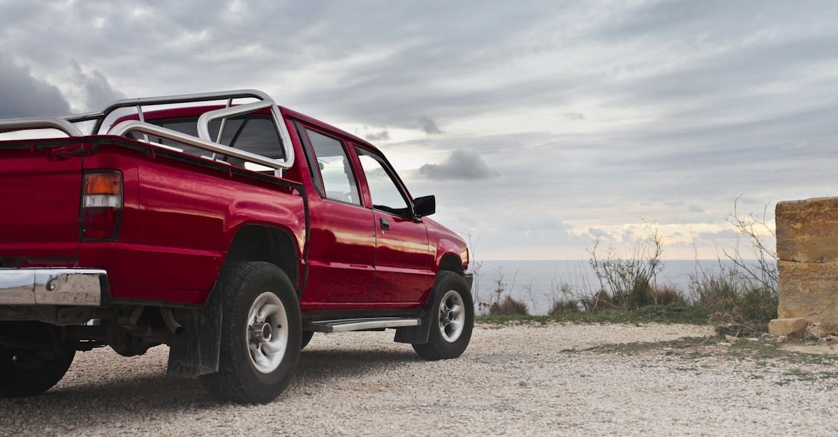 A red truck is parked on a gravel road near the ocean.