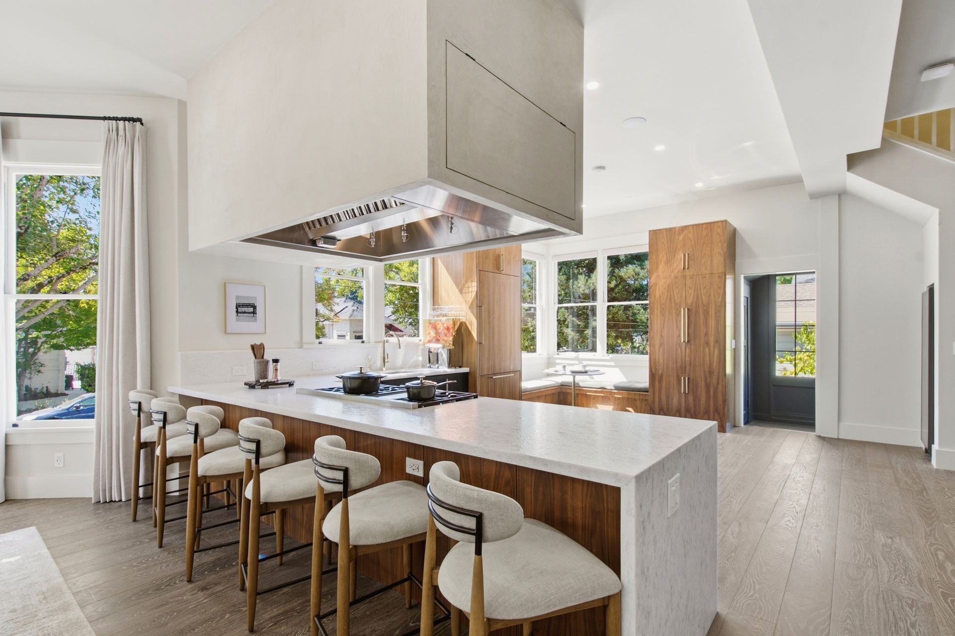 Bright modern kitchen with marble island, stools, and large windows overlooking greenery
